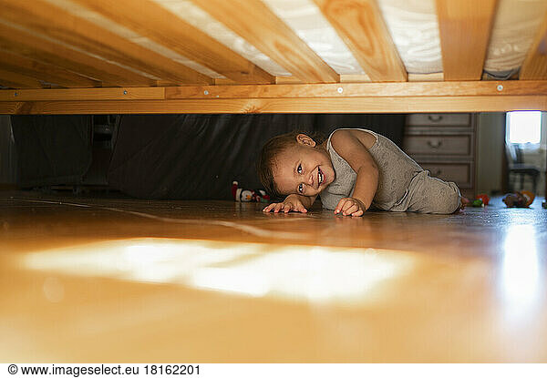 Happy boy looking under bed at home