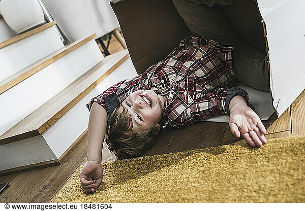 Happy boy lying on floor with cardboard box at home