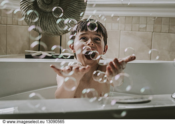 Happy boy playing with bubbles while taking bath in bathtub
