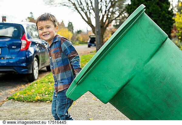 Happy boy pulling green trash can to street