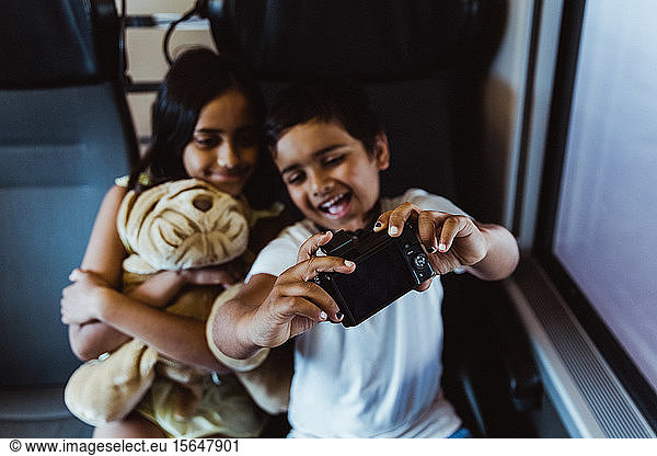 Happy boy taking selfie with sister on camera while traveling in train
