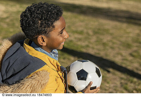 Happy boy wearing parka coat holding soccer ball in park