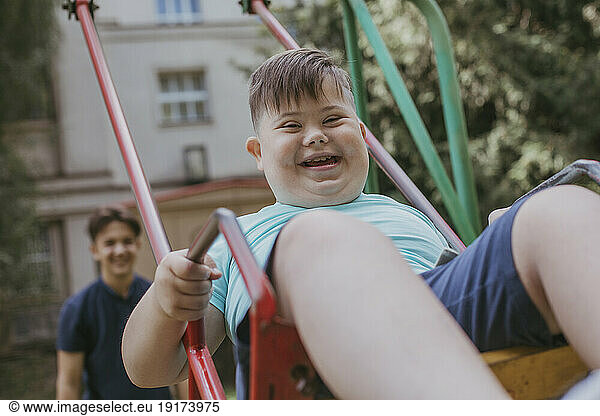 Happy boy with down syndrome playing on swing with brother in background