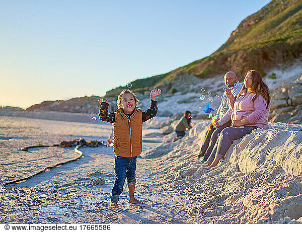 Happy boy with Down Syndrome playing with bubbles on sandy beach
