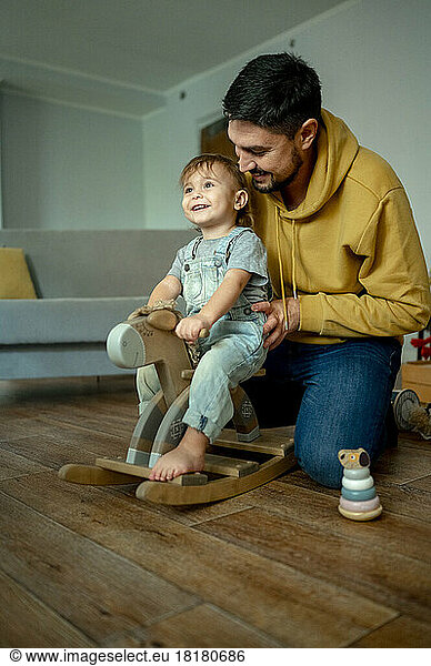 Happy boy with father playing on rocking horse at home