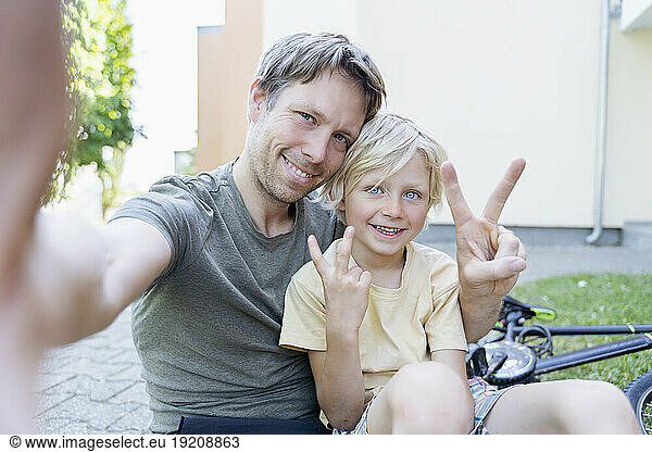 Happy boy with father taking selfie and gesturing peace sign