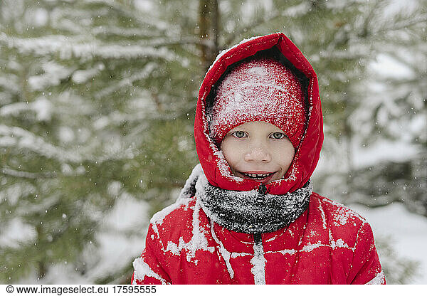 Happy boy with snow on knit hat and warm clothing in forest