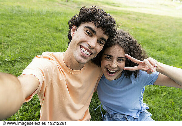 Happy boyfriend and girlfriend taking selfie on grass in park
