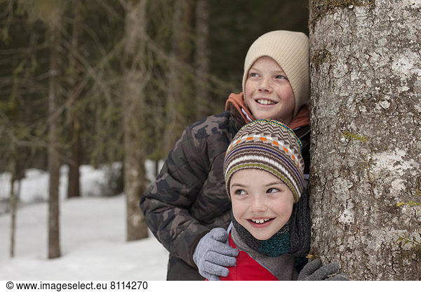 Happy boys leaning against tree trunk in snowy woods