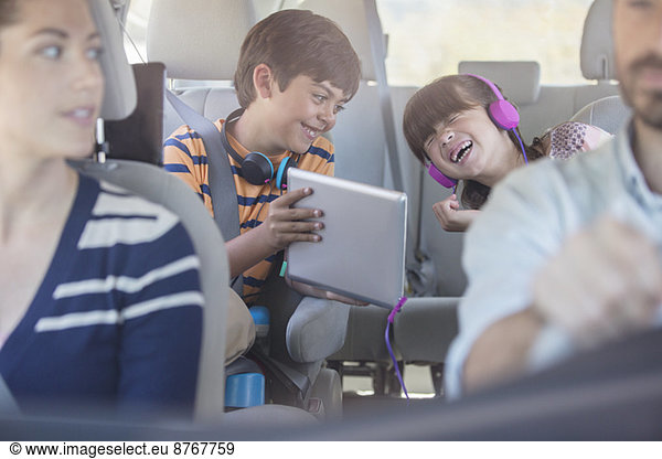 Happy brother and sister using digital tablet in back seat of car