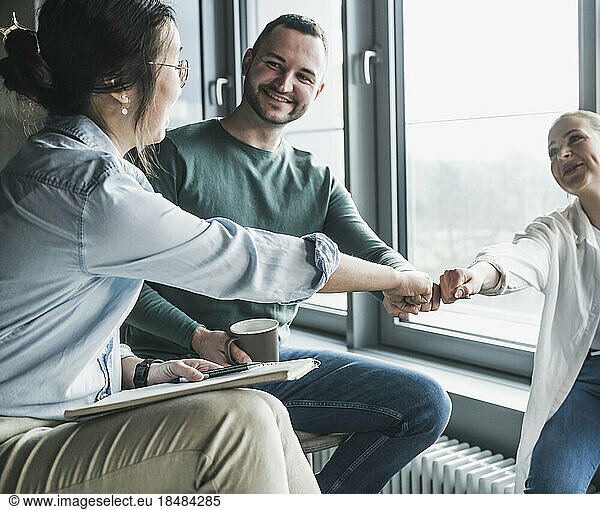 Happy business colleagues giving fist bump to each other at office