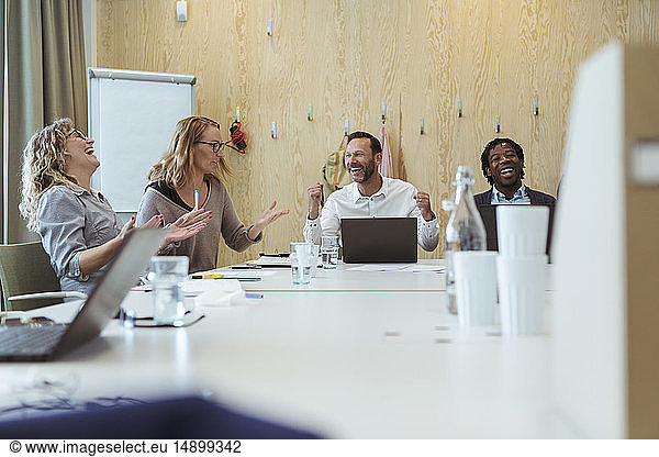 Happy business professionals cheering in meeting at office