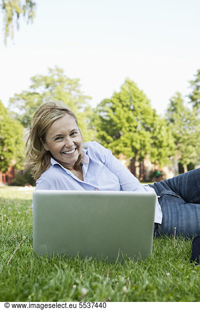 Happy business woman lying on side with laptop in park