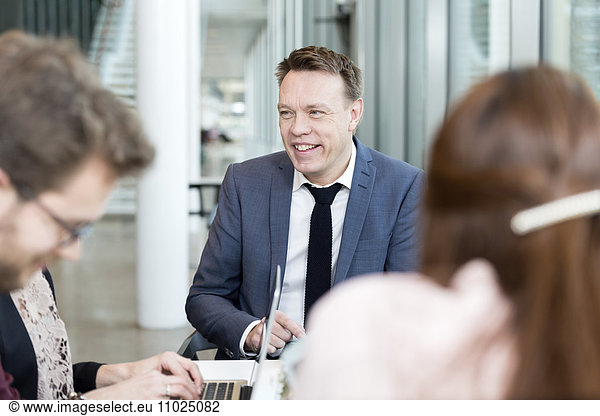 Happy businessman communicating with coworkers in meeting at office