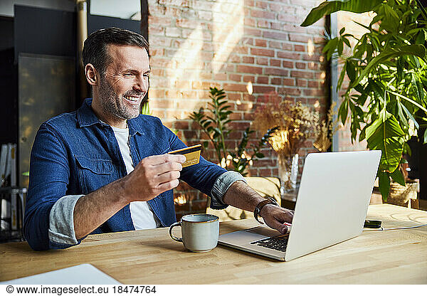 Happy businessman doing online shopping through credit card and laptop at loft office