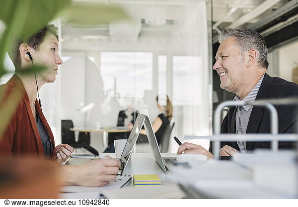 Happy businessman having discussion with colleague at desk