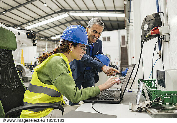 Happy businessman having discussion with colleague over laptop in factory