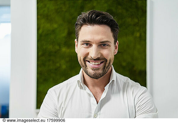 Happy businessman in front of wall at office
