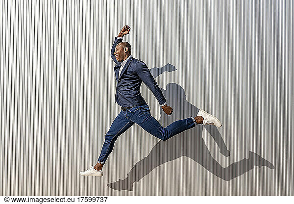 Happy businessman jumping in front of wall on sunny day