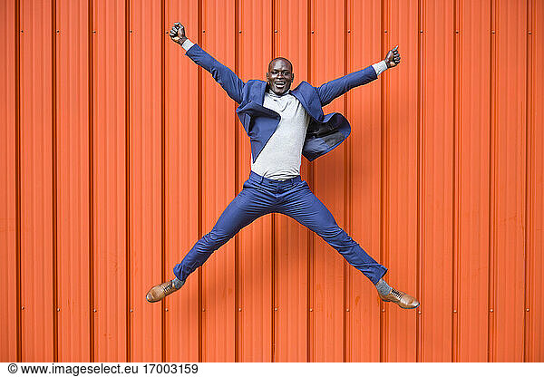 Happy businessman jumping in the air in front of orange wall