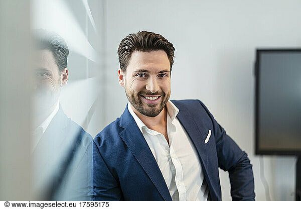 Happy businessman leaning on glass wall in office