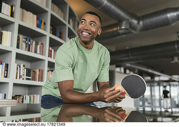 Happy businessman leaning on table with table tennis racket