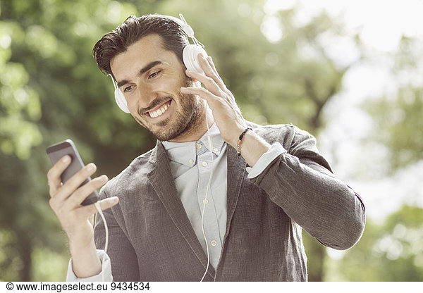 Happy businessman listening music though smart phone outdoors