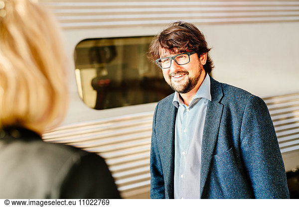 Happy businessman looking at female colleague on railroad station