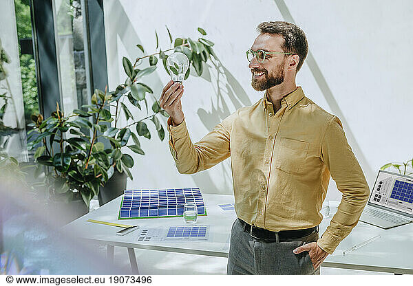 Happy businessman looking at light bulb in office