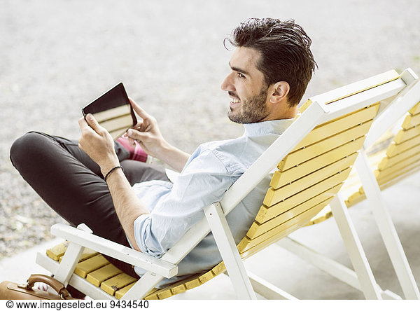 Happy businessman looking away while using digital tablet on lounge chair at park