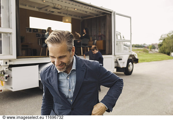 Happy businessman on road with colleagues and portable office truck in background