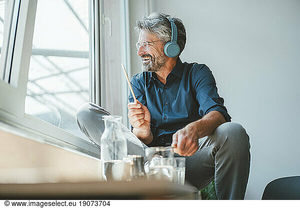 Happy businessman playing with sticks and listening music at office