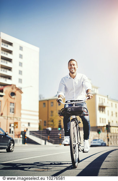 Happy businessman riding bicycle on city street against blue sky