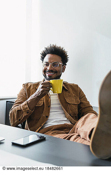 Happy businessman sitting with coffee cup in office