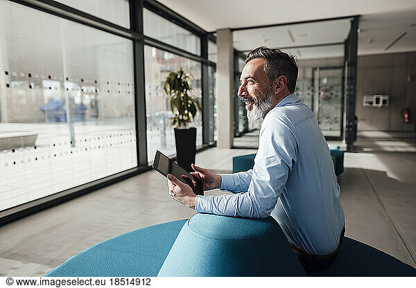 Happy businessman sitting with tablet PC in office