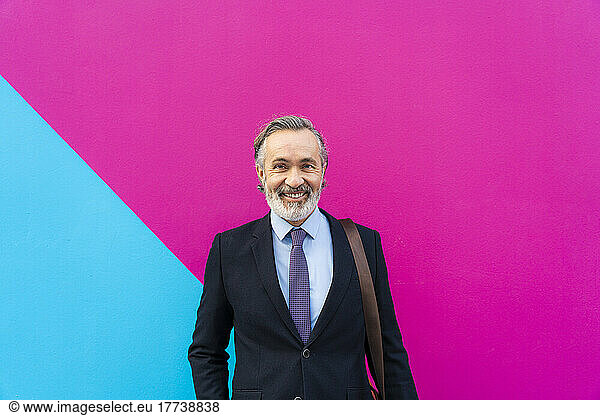 Happy businessman standing in front of pink and blue wall