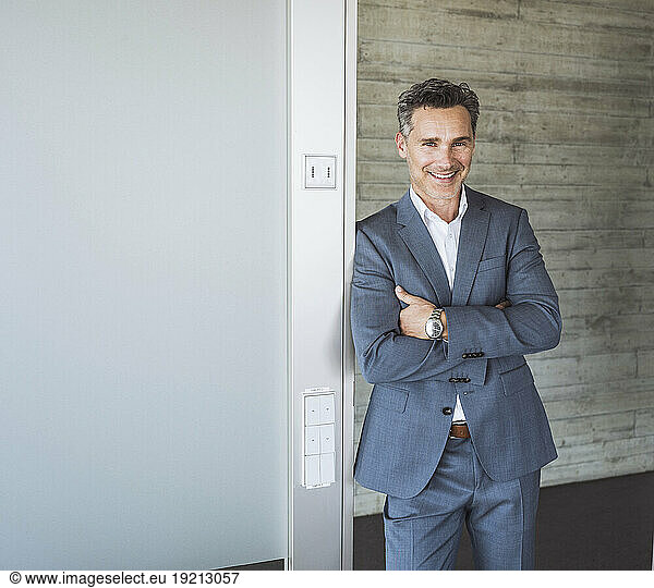 Happy businessman standing with arms crossed in front of wall