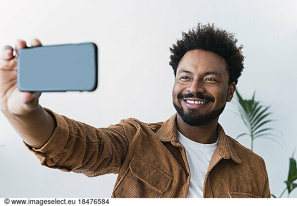 Happy businessman taking selfie with mobile phone in front of wall