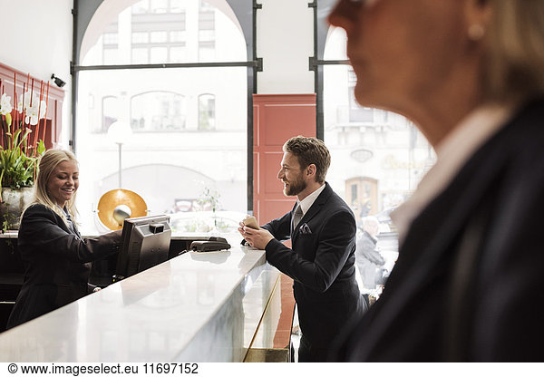 Happy businessman talking to female receptionist at hotel reception