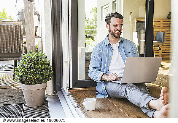 Happy businessman using laptop on floor in doorway