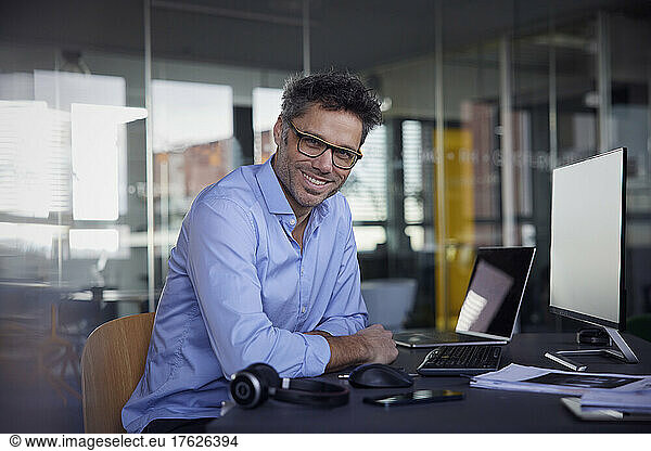Happy businessman wearing eyeglasses sitting at desk in office