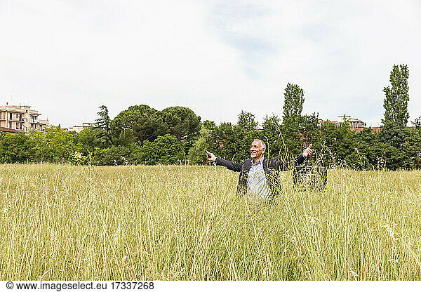 Happy businessman with arms outstretched standing in grassy field