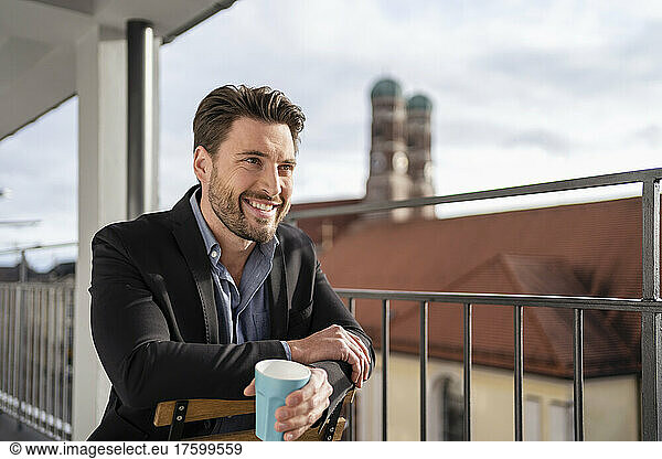 Happy businessman with coffee cup on office balcony