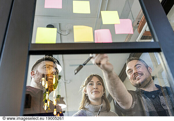 Happy businessman with colleagues discussing over adhesive notes