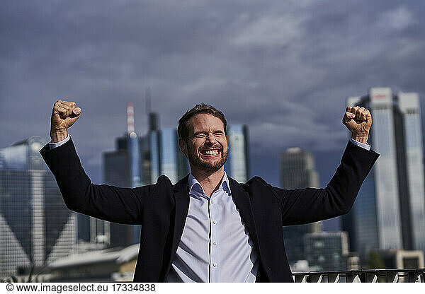 Happy businessman with hands raised at rooftop