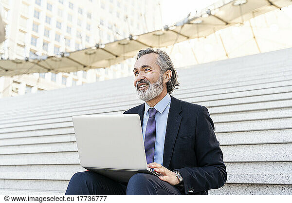 Happy businessman with laptop sitting on steps