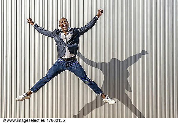 Happy businessman with mouth open jumping in front of white wall