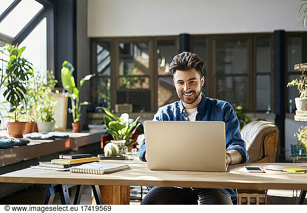 Happy businessman working on laptop at desk in office