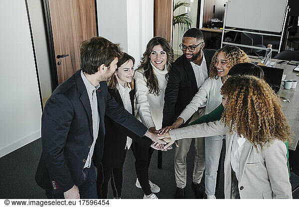 Happy businessmen and businesswomen stacking hands in coworking office