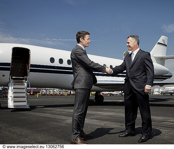 Happy businessmen doing handshake against corporate jet on runway